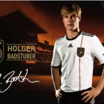 Ein männlicher Athlet in einem weiß-schwarzen Adidas-Sporttrikot steht selbstbewusst vor der Stadionkulisse, neben dem adidas-Logo und einem Deutschland-Schriftzug. Fritten, Fussball & Bier - www.soccer-warriors.de