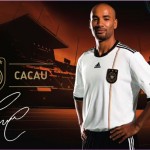 Ein Mann in einem weiß-schwarzen Deutschland-Fußballtrikot steht vor einem Stadionhintergrund mit Markenlogos und dem Namen „Cacau“. Fritten, Fussball & Bier - www.soccer-warriors.de