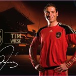 Fußballspieler in einem rot-schwarzen Torwarttrikot posiert für ein Werbebild mit Stadionlichtern im Hintergrund in Deutschland. Fritten, Fussball & Bier - www.soccer-warriors.de