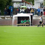 Spieler sitzen unter einem Schutzdach am Spielfeld, während ein Testspiel läuft. Fritten, Fussball & Bier - www.soccer-warriors.de