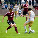 Fußballspieler in Aktion während eines Testspiels zwischen dem 1. FC Nürnberg und Racing Santander, einer im kastanienbraunen Trikot ist dabei, den Ball zu schießen, während ein Gegner im weißen Trikot zusieht. Fritten, Fussball & Bier - www.soccer-warriors.de