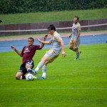 Zwei Fußballspieler von Racing Santander und dem 1. FC Nürnberg wetteifern bei einem Testspiel bei Regen um den Ball, im Hintergrund hält ein Zuschauer einen Regenschirm. Fritten, Fussball & Bier - www.soccer-warriors.de