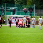Bei einem Testspiel zwischen Racing Santander und dem 1. FC Nürnberg versammelten sich Fußballspieler um einen verletzten Teamkollegen auf einem nassen Feld, im Hintergrund Zuschauer unter Sonnenschirmen. Fritten, Fussball & Bier - www.soccer-warriors.de