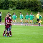 Ein Moment während eines Testspiels mit Spielern des 1. FC Nürnberg in Kastanienbraun und dem Torwart von Racing Santander im Einsatz, während Ersatzspieler und Trainer von der Seitenlinie aus zuschauen. Fritten, Fussball & Bier - www.soccer-warriors.de