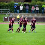 Fußballspieler in kastanienbraunen Uniformen feiern auf dem Spielfeld, im Hintergrund halten Zuschauer Regenschirme nach einem Testspiel zwischen dem 1. FC Nürnberg und Racing Santander. Fritten, Fussball & Bier - www.soccer-warriors.de