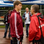 Zwei Personen unterhalten sich bei einer Testspiel-Freiluftveranstaltung mit Zuschauern und einem Weihenstephaner Markenzelt im Hintergrund. Fritten, Fussball & Bier - www.soccer-warriors.de