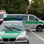 Auf einer Straße geparktes Polizeifahrzeug mit Notbeleuchtung, im Hintergrund ein Rettungshelfer mit Warnweste. Fritten, Fussball & Bier - www.soccer-warriors.de